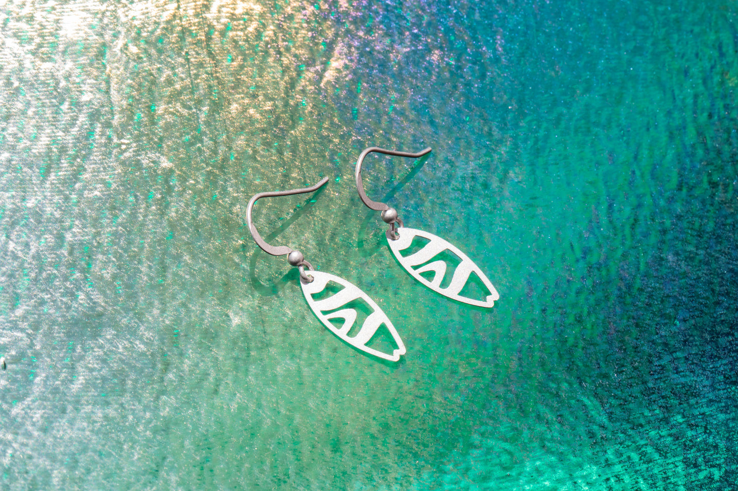 a pair of surfboard shaped earrings on shining blue background