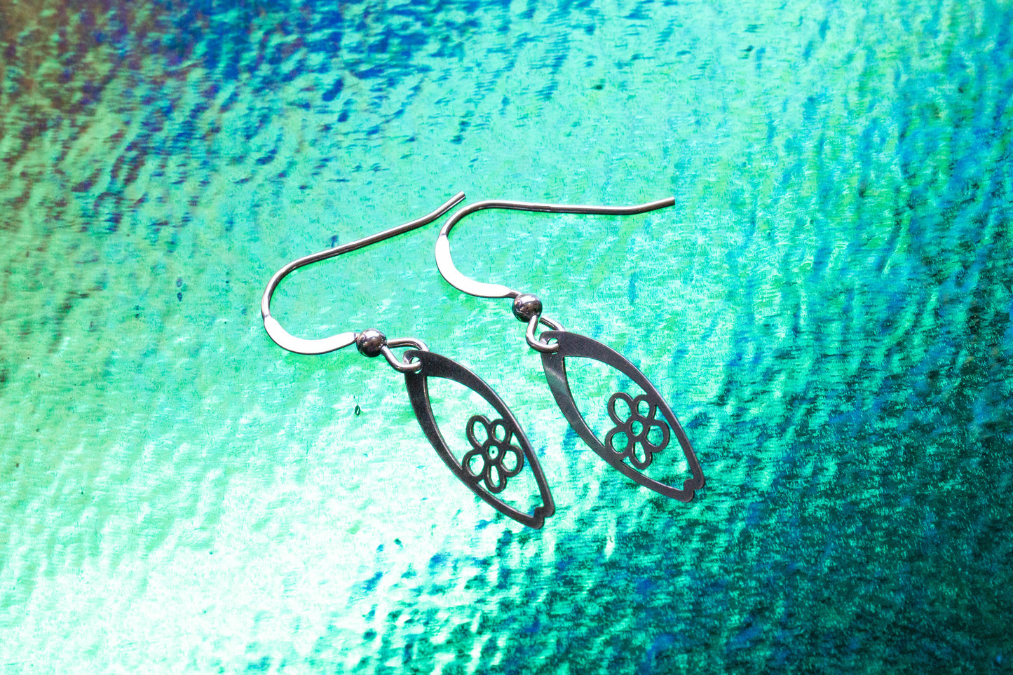 a pair of daisy flower surf inspired earrings on a breaking wave effect background