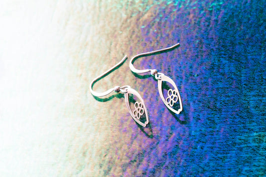 a pair of daisy flower patterned surfboard shaped earrings on a white fading to purple background