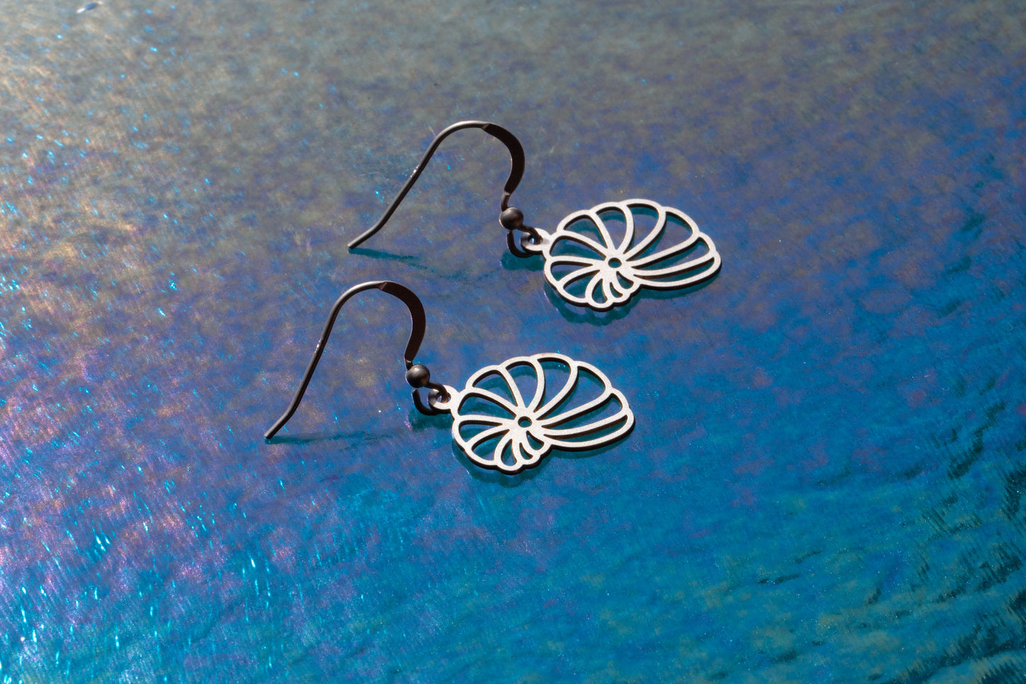 A pair of shell shaped sterling silver earrings on a purple background