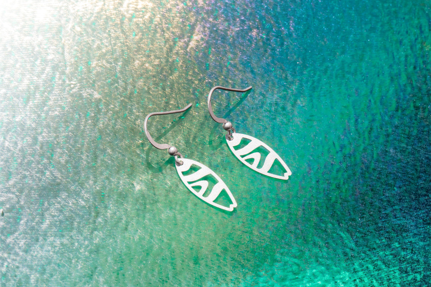 A pair of tiger stiped surfboard earrings on a sunshine flooded wave effect background