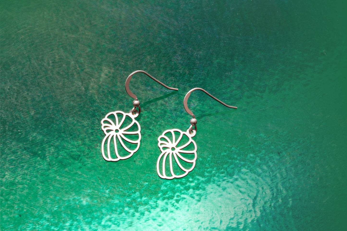 a pair of nautilus shell inspired sterling silver earrings on an ocean green background