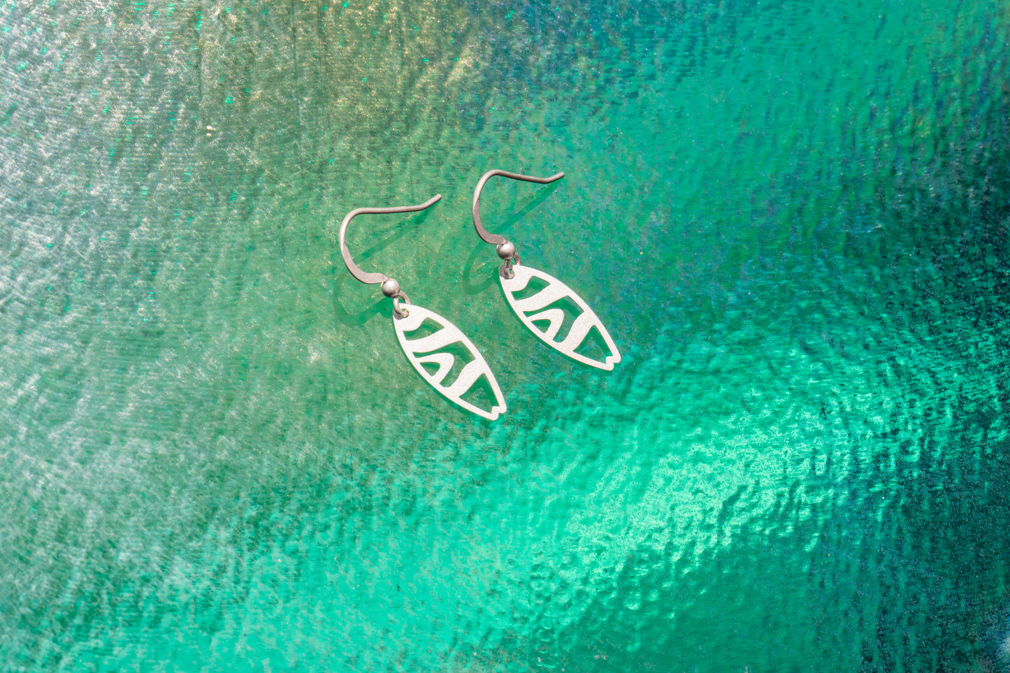 a pair of surfboard earings on a wave background