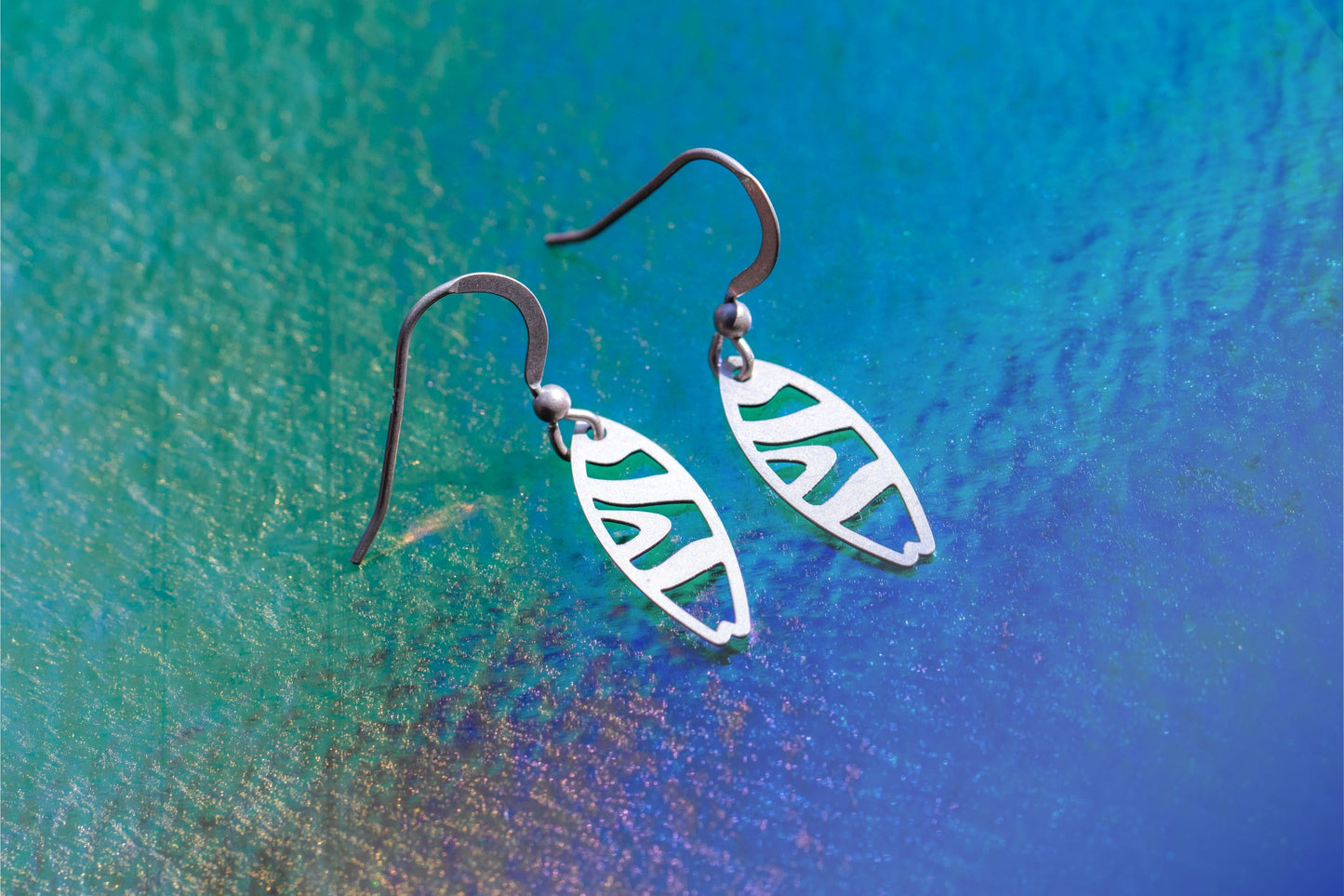 a pair of sterling silver earrings with a flowing stripe design on a deep blue wave background