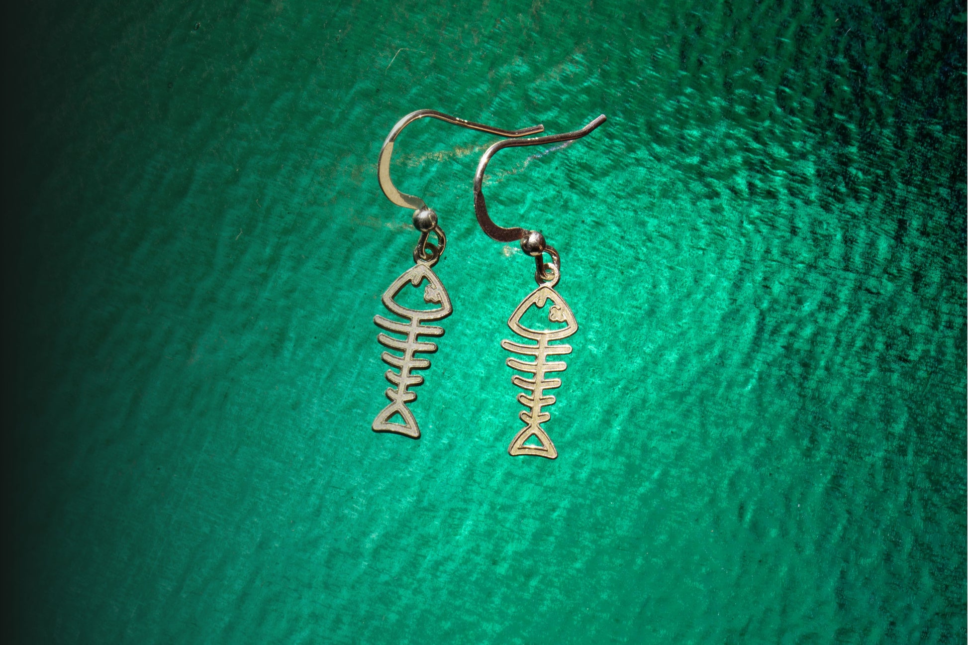 a Pair of sterling silver earrings shaped like fish above a deep sea background 