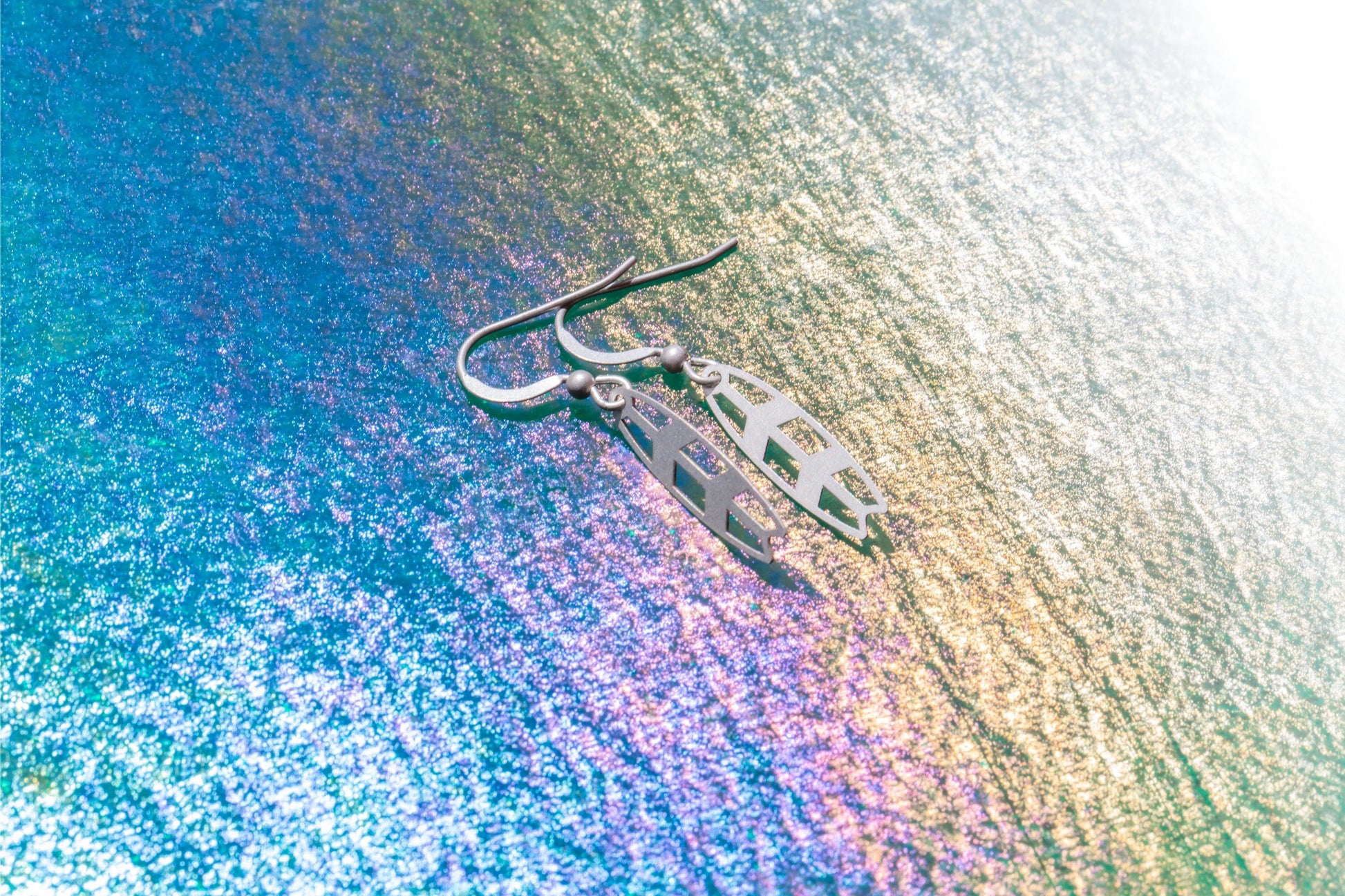 a pair of matt sterling silver surfboard earrings on a purple and white background