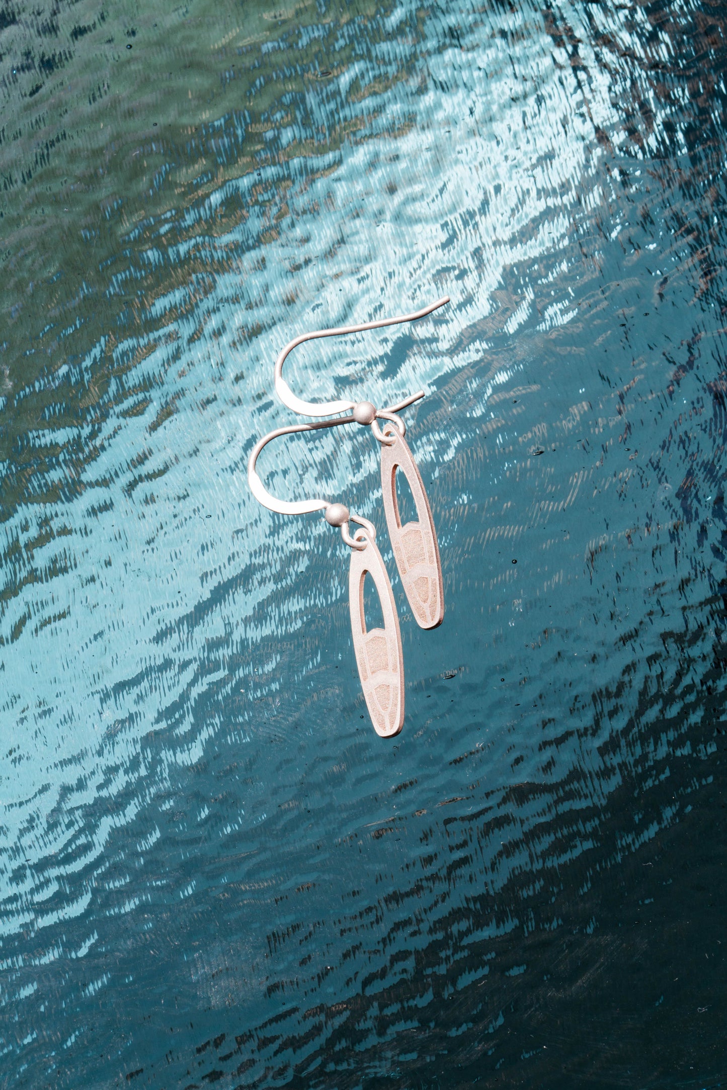 a pair of stirling silver surfboard earrings on a deep blue sea background