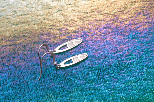Small  fun surfboard shaped earrings shown on a blue and gold iridescent background