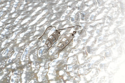 a pair of sterling silver earrings on a mirror like silver sea background 